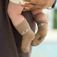 Baby wearing brown socks with white text held by a person, blurred background